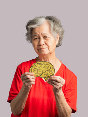 Portrait of a senior woman holding a brain symbol while standing on a gray background