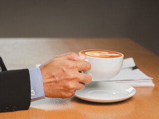 Businessman hand holding a cup of coffee sitting working at the office