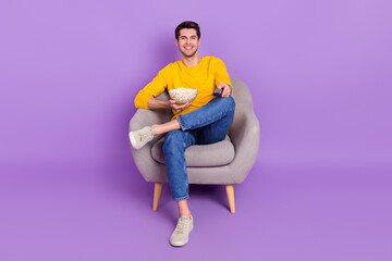 Full length image of good mood positive man sit chair watching tv after work eat popcorn isolated on violet color background