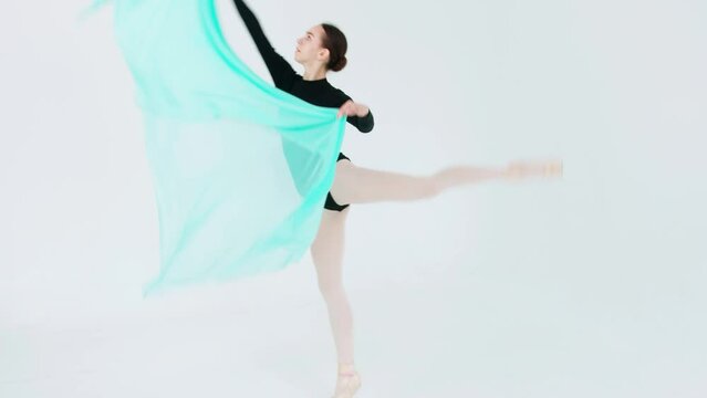 A graceful ballerina in a black leotard performs a fouette and an attitude with a fluttering turquoise veil in her hands