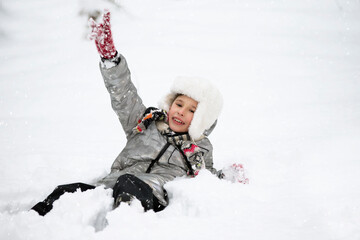 Fototapeta na wymiar A joyful boy in warm clothes lies in the snow. Child on a winter walk.