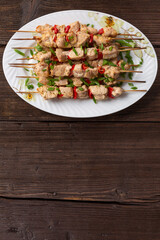 Meat kebabs on a large platter with sauces and herbs, wooden background with copy space