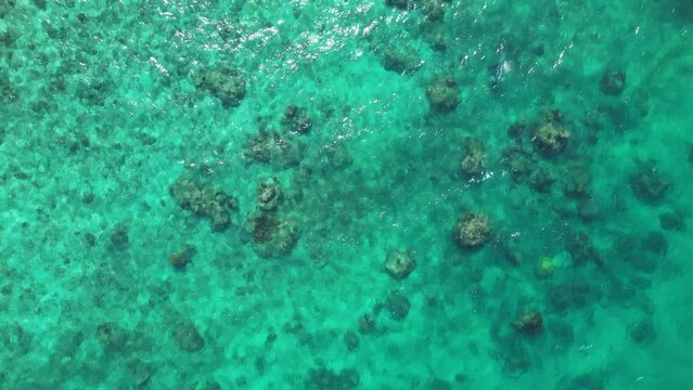 A drone is looking down on clear turquoise water flowing over rocks.