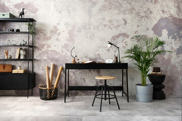Concrete interior of home office with black desk, copy space, office accessories, lamp. Rack with personal accessories. Home decor. Template.
