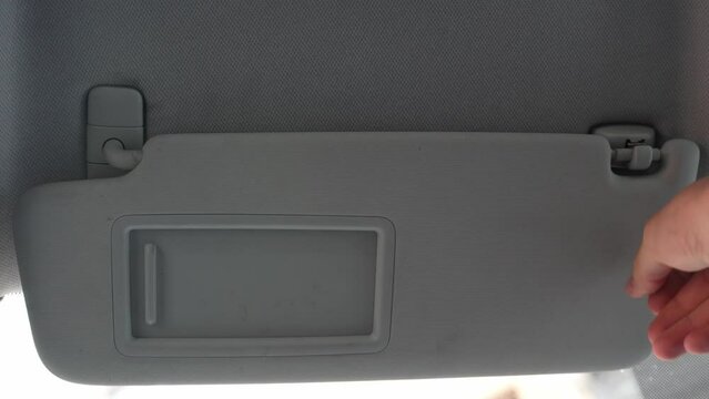 Man's hand flip up sun visor and slide mirror, car interior scene, close up