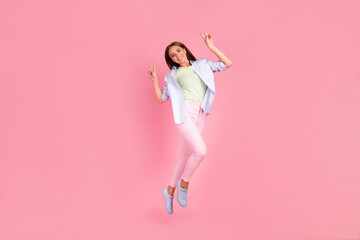 Full size portrait of cheerful pretty young girl jumping arms demonstrate v-sign isolated on pink color background
