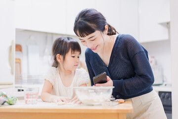 Fototapeta premium ママとスマホでレシピを見ながら料理をする娘