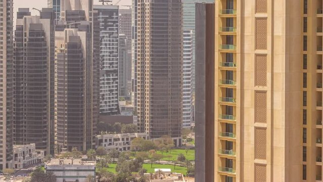 Skyscrapers at the Business Bay in Dubai aerial timelapse during all day with shadows mobing fast. Green lawn with palms in the yard, United Arab Emirates