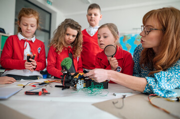 Group of kids with their teacher programming electric toys and robots at robotics classroom