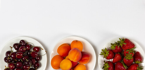 Three plates with ripe summer fruits and berries on white background, top view and copy space
