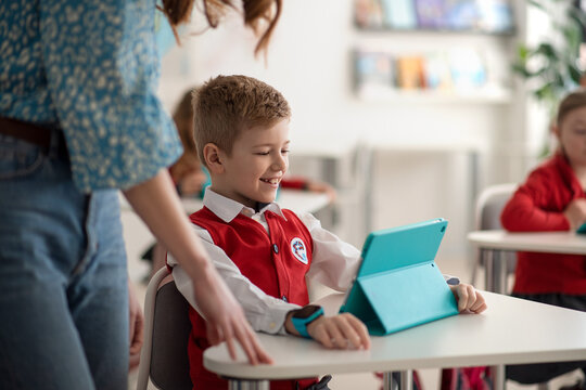 Happy schoolboy using digital tablet during lesson in classroom at primary school.