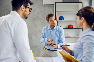 Obraz premium A main architect manages project on tablet in the office and talking to the colleagues.