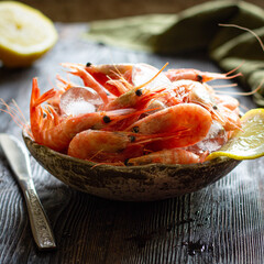 Frozen shrimps with lemon and ice on a dark wooden table.