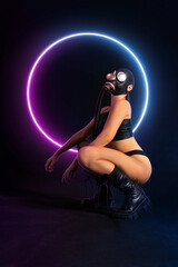 Seductive girl fetish model with a slim figure poses sitting in a black gas mask, black leather or...