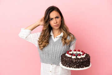 Young woman holding birthday cake over isolated pink background having doubts