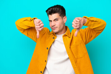 Young handsome caucasian man isolated on blue bakcground showing thumb down with two hands