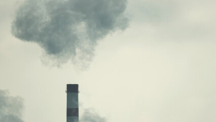 Smoke is coming from the chimney of the power plant. In the background is a gray sky covered in...