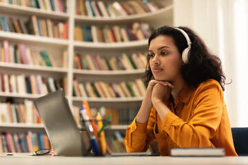 Pensive student lady looking at laptop computer, learning online, having remote class with distant teacher, sitting in library