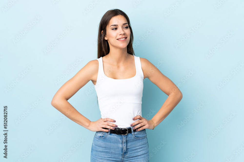 Canvas Prints Young caucasian woman isolated on blue background posing with arms at hip and smiling