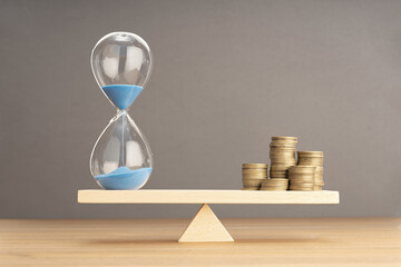Balance Between Time and money concept. Sand clock and stacked coins on Seesaw. Copy space