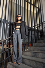 Fashionable concept, Fashion woman is posing in sunglasses and pants with white shirt on the stairs