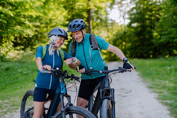 Plakat Portrait of active senior couple riding bicycles at summer park, looking at sports smartwatch, checking their performance.