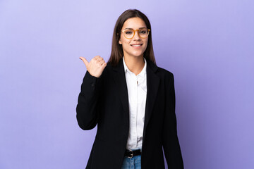 Business woman isolated on purple background pointing to the side to present a product