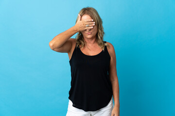 Middle aged blonde woman over isolated background covering eyes by hands. Do not want to see something