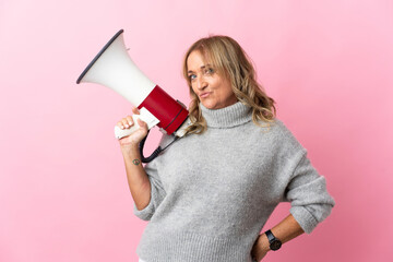 Middle aged blonde woman over isolated pink background holding a megaphone and thinking