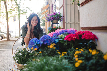 Young urban woman looking at flowers at street shop on sunny day in summer.