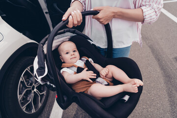 Fototapeta na wymiar Cropped portrait of mother hands hold toddler sitting safety chair street outside car salon