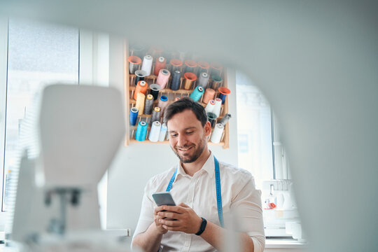 Smiling Male Tailor Messaging On Smartphone At Workplace