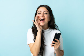 Young woman using mobile phone isolated on blue background shouting with mouth wide open