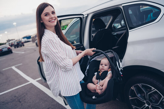 Photo of pretty charming mommy little son dressed casual clothes putting car seat inside auto transport open door