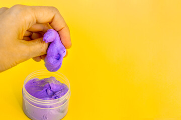 A woman's hand crumples purple rubber taken out of a jar on a bright yellow background. An anti-stress toy. Copy space