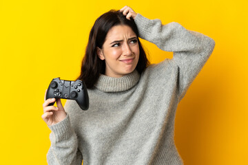 Woman playing with a video game controllerisolrted on yellow background having doubts and with...