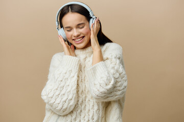 a happy, beautiful woman poses relaxed standing on a background with headphones and gently touches her hands with her eyes closed with pleasure