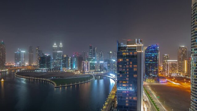 Cityscape of skyscrapers in Dubai Business Bay with water canal aerial night timelapse. Modern skyline with illuminated windows in towers at waterfront. A center of international business