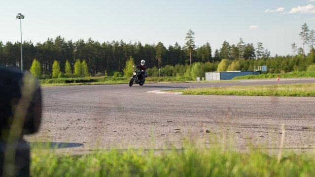 Biker on motorbike riding turn on forest race track, then wave by hand
