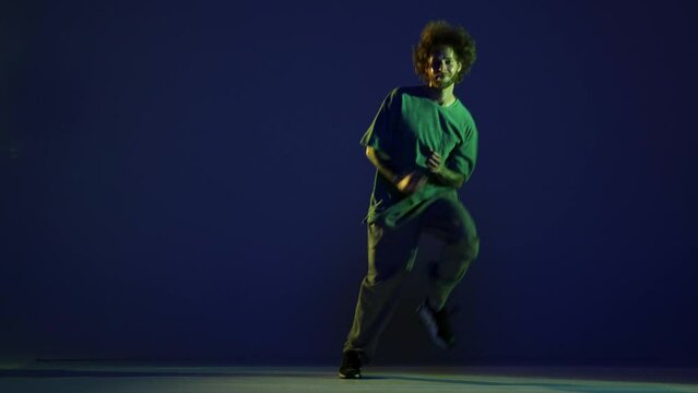 Stylish young man, hip-hop dancer dancing isolated over dark blue background in neon light. Modern dance art, fashion, youth, ad, style. 4K, video