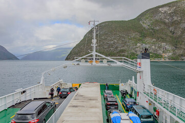 View of a typical Norwegian fjord landscape from a ferry upper deck. Blue sea water, cloudy sky and misty mountains. vehicles on the deck