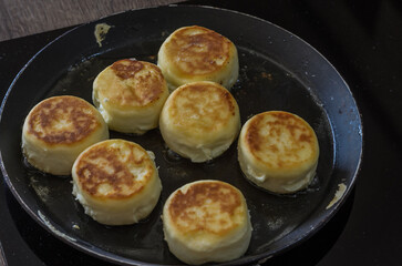 The cook prepares a morning breakfast, syrniki in a frying pan on an induction stove	