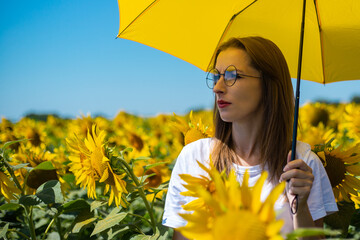 Young woman under yellow umbrella at sunflower field