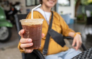 Someone holding a plastic cup of iced Americano (black coffee). 