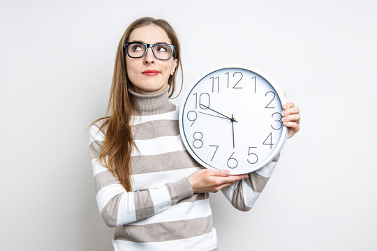 Young woman pensive looking up holding a clock on a light background.