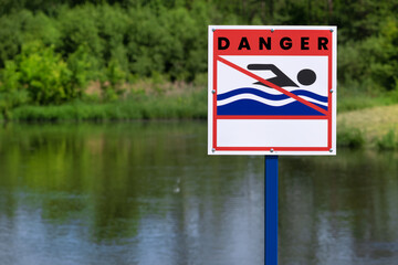 Swimming sign, on the river bank. Sign on the shore of the reservoir: swimming is prohibited. Grass and summer day. The sign informs you that you cannot swim here