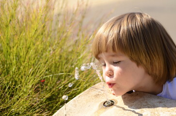 Drinking fountain. Water jet. Little boy greedily drinks water on a hot sunny day