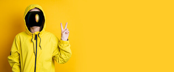 A young woman in a mask of cyberpunk goggles in a yellow jacket shows a peace victory sign on a yellow background. Banner