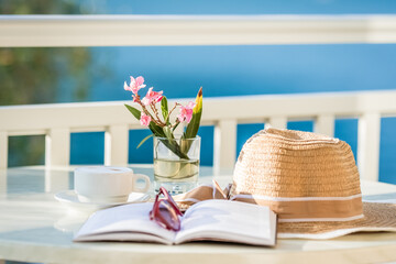 Fototapeta Kapelusz słoneczny oraz książka leży na stoliku na balkonie w pokoju hotelowym z balkonem obraz