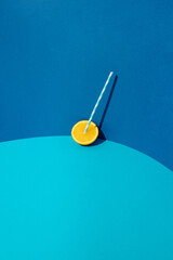 Halved orange with white - blue paper drinking straw leaning against a blue wall. Summer minimal concept.